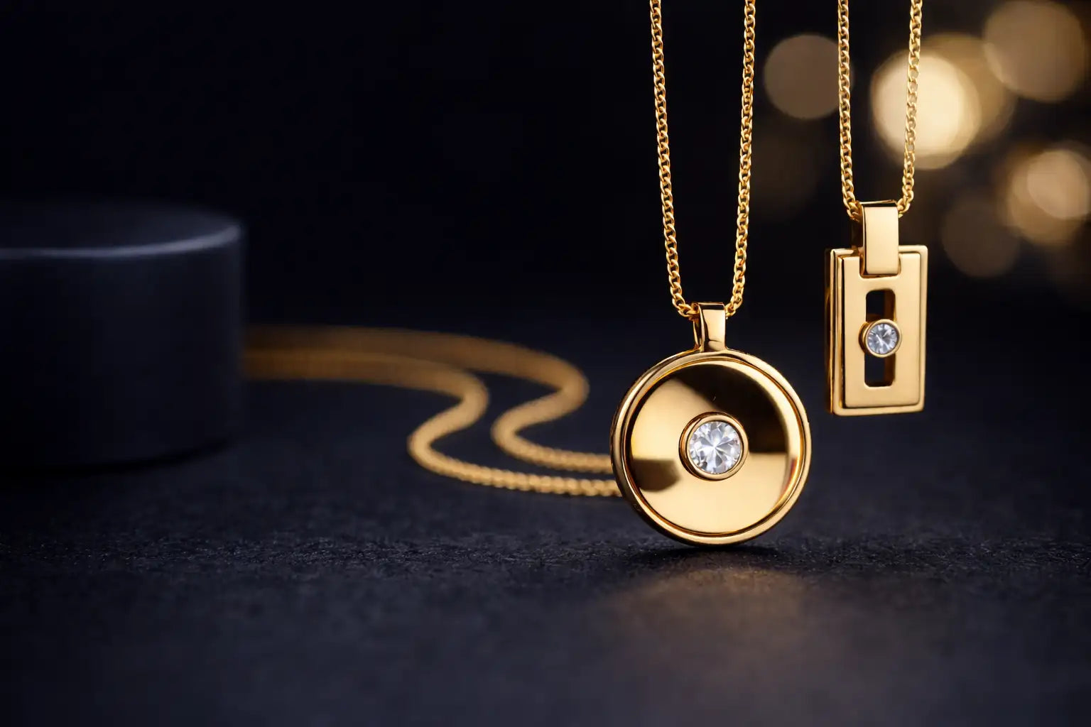 Golden pendant necklaces featuring a round disc and rectangular design, each centered with a sparkling diamond.